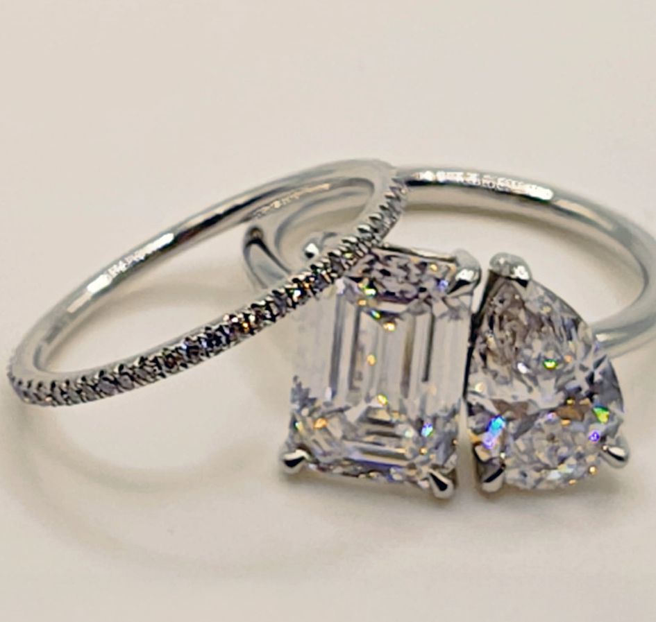 Three rings are shown: a thin diamond eternity band, an emerald-cut diamond ring, and a pear-shaped diamond ring, all set in white metal and displayed against a plain white background.