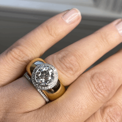 A manicured hand wears three dome rings: a thin pavé diamond band, a wide gold band, and a round halo diamond engagement ring.
