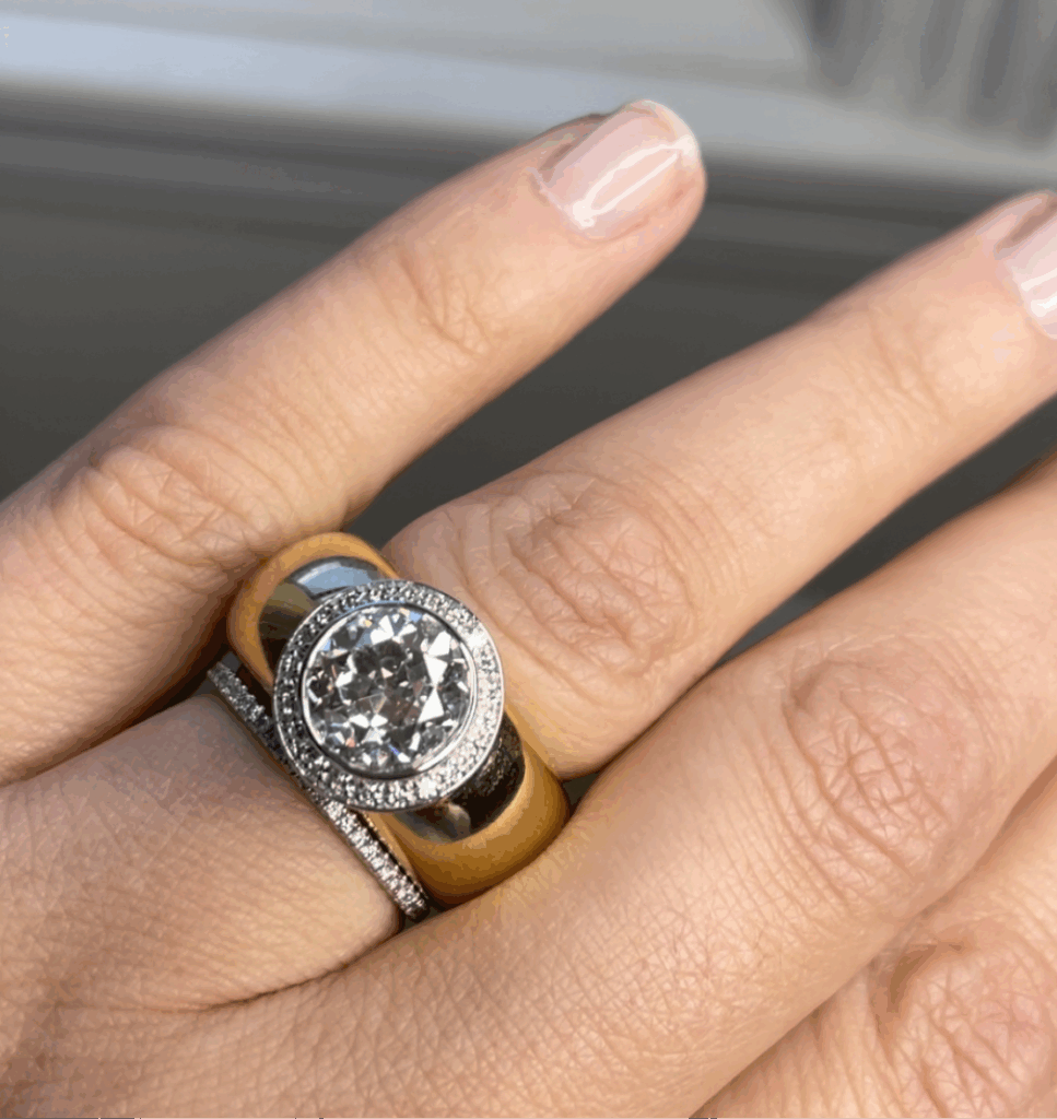 A manicured hand wears three dome rings: a thin pavé diamond band, a wide gold band, and a round halo diamond engagement ring.