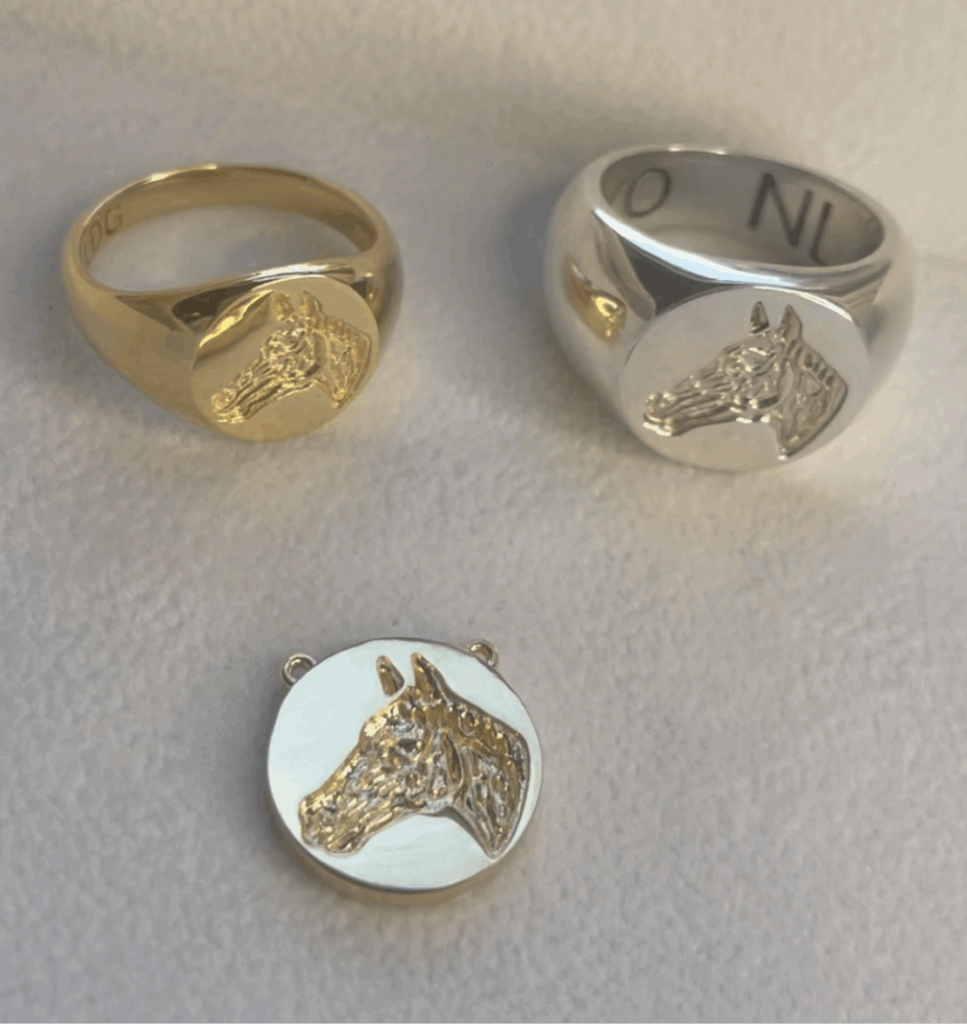 The Equestrian Line features gold and silver signet rings with a matching round pendant, each engraved with a detailed horse head, displayed on a light surface.